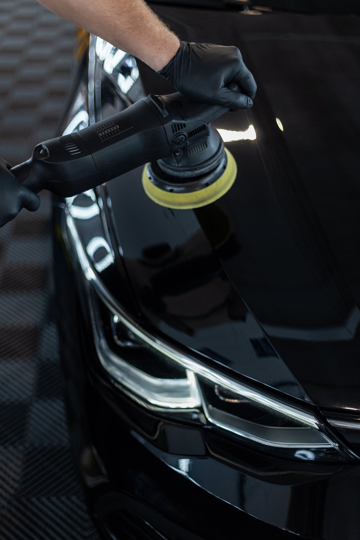 Detailer polishing a black car in a moody studio